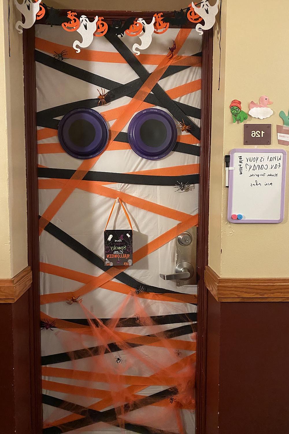 A dorm door covered in orange and black ribbons and two purple eyes.